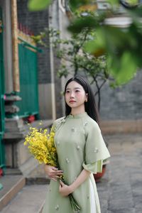 Graceful Vietnamese girl in green Ao Dai with yellow flowers at sacred pagoda-2